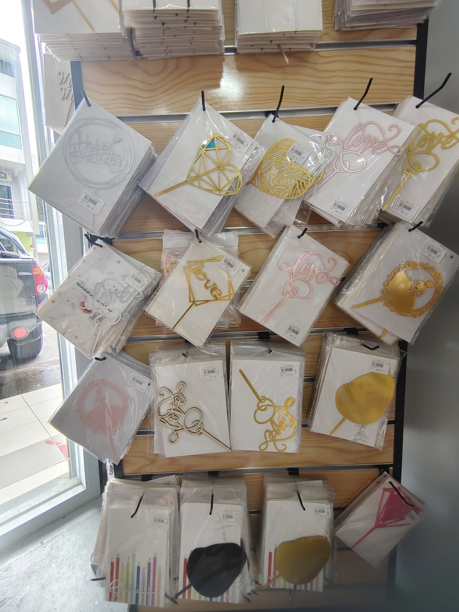 Wall display of acrylic love and heart-shaped cake toppers for sale inside the shop
